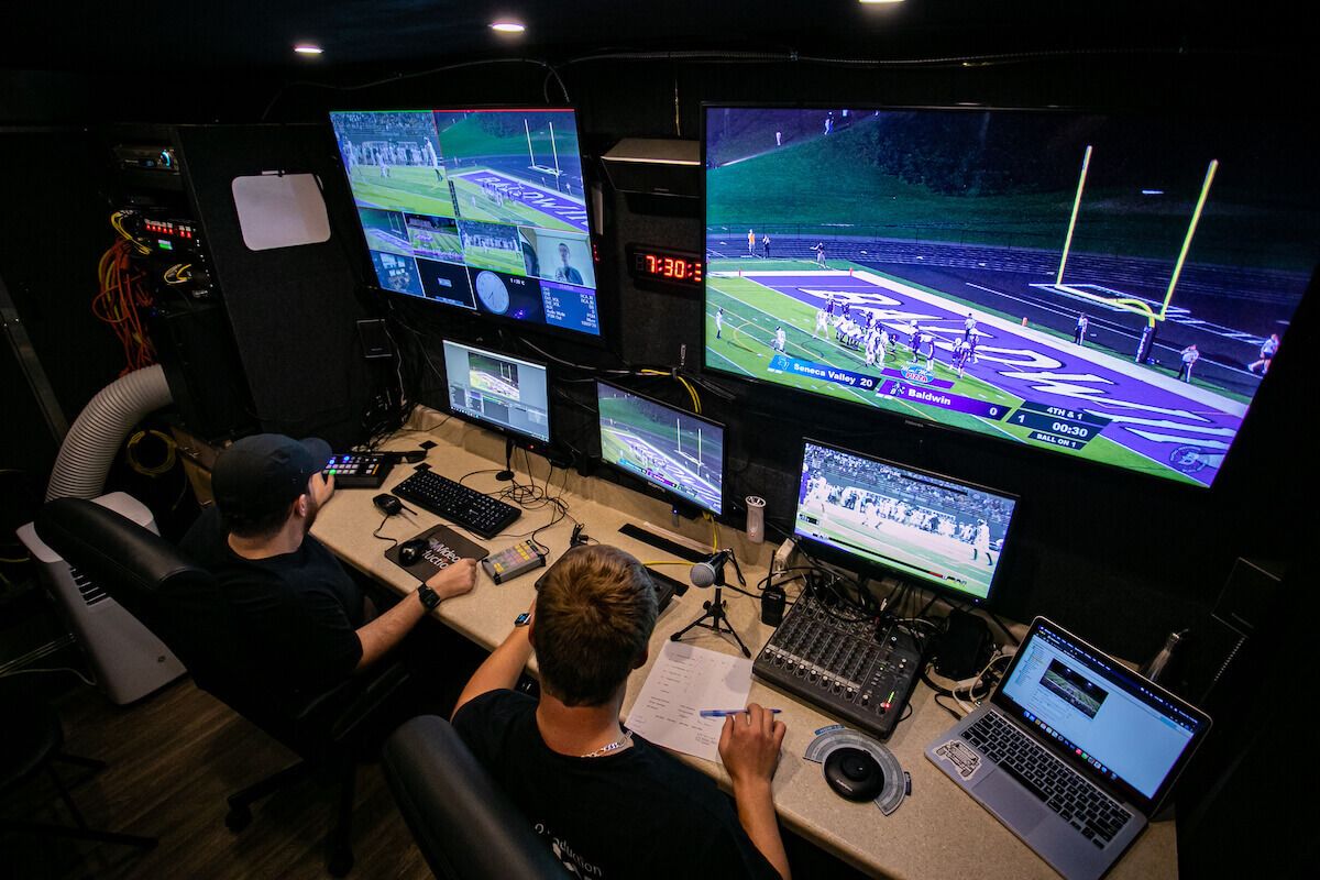 Two men sitting in front of multiple monitors broadcasting a sporting event